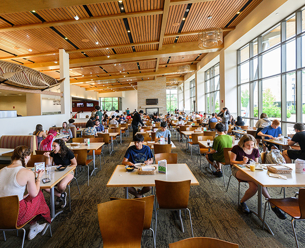 A crowded, brightly-lit dining hall filled with students eating lunch.